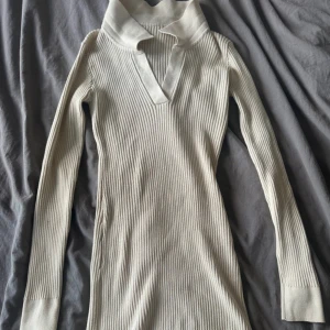 Beige ribbad klänning från SHEIN - Snygg beige ribbad klänning från SHEIN i figurnära modell. Klänningen har lång ärm, v-ringning och hög krage med cool detalj framtill. Perfekt för dig som gillar stilrena och trendiga plagg med en twist.