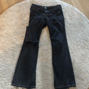 Svarta bootcut jeans med slitningar - Svarta jeans med bootcut passform och slitna detaljer på låret och knät. Jeansen har klassisk femficksdesign och dragkedja med knapp. Perfekta för dig som gillar en edgy och avslappnad stil. Skit snygga!