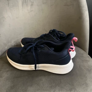 Mörkblå sneakers från Rugged Gear - Snygga mörkblå sneakers från Rugged Gear med vit och rosa sula. Ovandelen är i mesh och syntet, vilket ger en sportig vibe. Skorna har snörning och rosa detaljer på häl och sula. Perfekta för dig som gillar stilrena och bekväma sneakers.