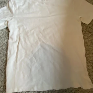 Vit t-shirt från SMOG relaxed fit - Enkel och stilren vit t-shirt från SMOG i relaxed fit. T-shirten har rund halsringning och korta ärmar, perfekt för en clean och avslappnad look. Materialet känns mjukt och skönt mot huden.