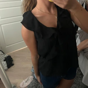 Svart topp med volangdetaljer - Supersnygg svart topp med volang längs v-ringningen och axlarna. Den är från Zara i storlek S. 