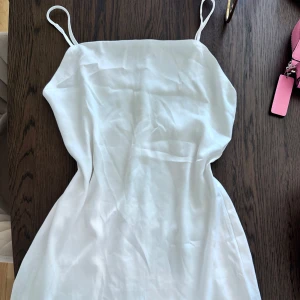 Vit somrig klänning med smala band - Superfin vit klänning med smala axelband och enkel, rak passform. Perfekt för varma dagar och har en lätt, flowy känsla. Stilren och minimalistisk design som är lätt att matcha med accessoarer.