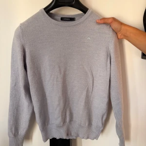 Ljusgrå stickad tröja J.Lindeberg - Jag säljer min ljusblå stickad tröja från J.Lindeberg med diskret logga på bröstet. Tröjan har rund halsringning, Perfekt för lager-på-lager och enkel att matcha. Tröjan är gjord av merinoull, på bilderna ser tröjan lila ut men den är babyblå irl. Hör av dig vid frågor.
