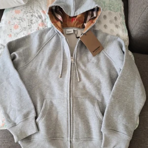 Grå hoodie från Burberry, Storlek L men passar perfekt för M - Snygg grå hoodie från Burberry med hel dragkedja, huva med snörning och broderad logga på bröstet. Pris kan diskuteras