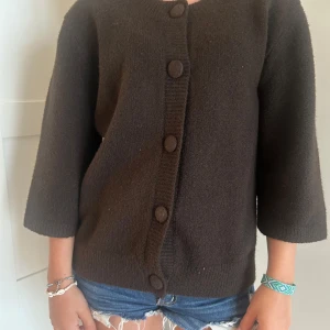 Brun kofta från Neo Noir - Mysig brun kofta från Neo Noir med stora matchande knappar framtill. Koftan har trekvartsärmar och är stickad i ett mjukt material. Perfekt för lager-på-lager och chill dagar. Enkel och stilren design som funkar till det mesta.