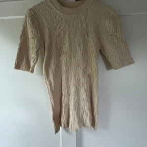 Beige ribbad topp från Selected Femme - Säljer en beige ribbad topp från Selected Femme. Toppen har en rund halsringning, korta ärmar och en strukturerad, stretchig känsla💗