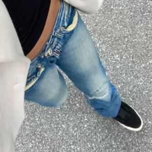 Blå Replay jeans med broderi - Säljer ett par blå Replay jeans med coola detaljer som broderade fickor och slitningar baktill. Jeansen har låg midja, klassisk femficksdesign. Materialet är jeans med snygg tvätt och gul söm. Storlek w27 L34