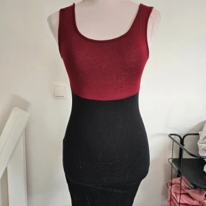 Röd och svart tight klänning - Snygg tvåfärgad klänning med vinröd överdel och svart kjoldel. Ärmlös och figurnära modell med rund halsringning. Tillverkad i stretchigt material av viskos och elastan, perfekt för dig som gillar en slim passform.
