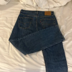 Levi's 501 blå jeans W32 L32 - Klassiska Levi's 501 jeans i blå denim med raka ben och normal passform. Byxorna har fem fickor, knappgylf och den ikoniska läderpatchen bak i midjan. Perfekta för dig som gillar tidlös stil och vill ha ett par schyssta jeans i bomull. Använda ett fåtal gånger och em perfekt mörk fin färg nu i för hösten. Hör ev er vid minsta fundering😊
