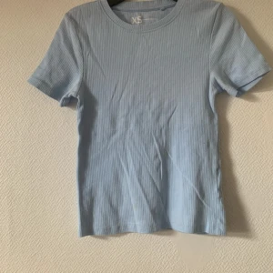 Ljusblå ribbad t-shirt XS - Snygg ljusblå t-shirt i ribbad bomull med korta ärmar och rund hals. Enkel och fräsch design som är lätt att matcha med jeans eller kjol. Perfekt för dig som gillar stilrena och bekväma plagg med lite struktur.