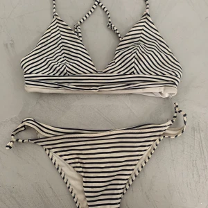 Randig bikini med knyt i midjan - Snygg bikini med svartvita ränder och smala axelband. Överdelen har triangelformade kupor och underdelen har knyt i sidan för en justerbar passform. Perfekt för stranden eller poolen.