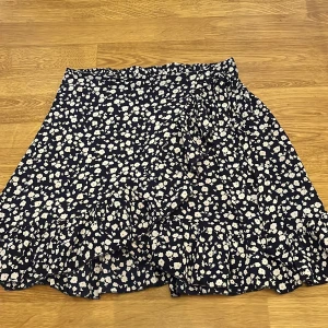 Blommig omlottkjol från SHEIN XS - Supersöt kort omlottkjol från SHEIN i marinblått med vita blommor. Kjolen har volangkant och knytband i midjan för extra detalj. Perfekt för dig som gillar en feminin och trendig stil.