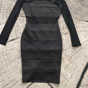 Svart meshklänning från Dennis Maglic - Nypris är 500kr Snygg svart kortklänning från Dennis Maglic med meshdetaljer upptill och långa ärmar. Klänningen har en tight passform och horisontella paneler som ger en cool look. Perfekt för dig som vill sticka ut med en stilren och modern outfit.