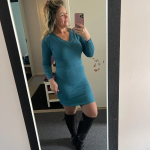 Turkos stickad kortklänning - Supersnygg mörk grön stickad klänning med v-ringning och lång ärm. Modellen är tight och kort, perfekt att styla med höga boots. Mjuk och stretchig känsla, passar dig som gillar en enkel men ändå trendig look.Bomull 