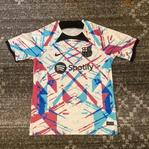 Barcelona x Nike kortärmad fotbollströja 23/24 - Säljer en Barcelona x Nike fotbollströja med Spotify-logga. Tröjan är vit med ett fett grafiskt mönster i blått och rött, har svart krage och detaljer. Materialet är lätt polyester, perfekt för träning eller match. FCB-emblem och Nike Swoosh i svart på bröstet. Träningströja från säsongen 23/24. Priset kan diskuteras.