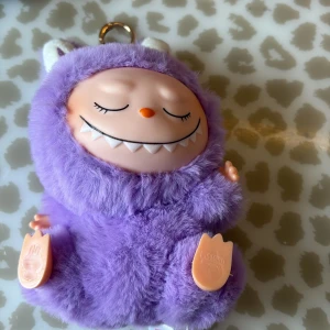 Lafufu have a seat. Lila 💜  - Supergullig nyckelring från Pop Mart i form av ett litet monster med lila fluffig päls, vita öron och ett sött ansikte med stängda ögon och vassa tänder. Perfekt att hänga på väskan med den lilla ringen upptill. Unik accessoar för dig som gillar kawaii-stil!