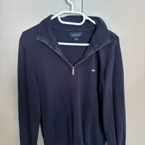 Mörkblå half zip tröja Lexington - Mörkblå långärmad tröja från Lexington med ribbad krage och half zip-dragkedja. Klassisk och stilren design med liten Lexington-logga på bröstet. Perfekt för dig som gillar en enkel men snygg look.