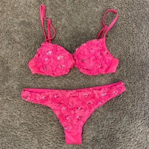Rosa calzedonia bikini - Superfin rosa bikini med blommor och glittriga paljetter på både överdel och underdel. Bikinin har smala axelband och bygel. Underdelen är ej använd och överdelen är använd ett fåtal gånger. Överdelen passar en A kupa