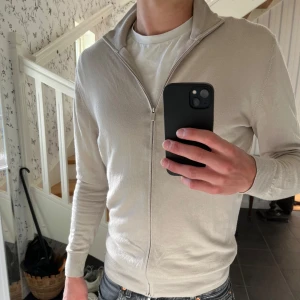Beige merinoullskofta från Boggi Milano - Snygg beige kofta från Boggi Milano i superfin merinoull. Modellen har hel dragkedja framtill, hög krage och ribbade muddar. Endast använd ett fåtal gånger och i superfint skick! Nypris 2650kr