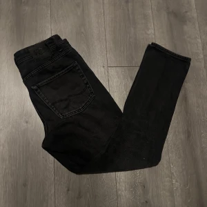 jeans från Jack & Jones - Säljer ett par svarta jeans från Jack & Jones med klassisk femficksdesign och rak passform. Jeansen har en mörk tvätt och är tillverkade i slitstarkt denimtyg. Perfekt för dig som gillar en enkel och stilren look.