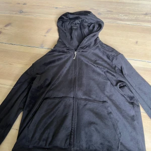 Svart velour hoodie Juicy Couture - Svart hoodie från Juicy Couture i mjuk velour med dragkedja och klassisk J-detalj på zippen. Tröjan har huva, två fickor fram och långa ärmar.  Inte använd alls mycket så nyskick, org pris 899kr
