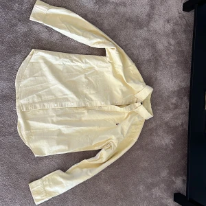 Ralph lauren skjorta  - Jag säljer en gul Ralph lauren skjorta som är använd 1 gång. Inga fläckar eller hål. 
