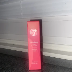 W7 Gloss Away Lip Balm Strawberry - Säljer ett W7 Gloss Away Lip Balm i smaken Strawberry. Kommer i en snygg rosa förpackning och ger läpparna en fräsch glans med en hint av jordgubb. Perfekt att ha i väskan för återfuktade och mjuka läppar hela dagen.