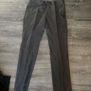 Grå kostymbyxor från Erla of Sweden - Snygga grå kostymbyxor från Erla of Sweden Exclusive Collection. Klassisk rak passform med pressveck och diskreta fickor. Perfekt för dig som vill ha en stilren och dressad look. Materialet känns mjukt och har en elegant finish.