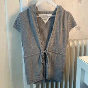 Grå stickad väst med huva Hilfiger - Mysig grå stickad väst från Hilfiger Denim med korta ärmar, huva och knytband framtill. Västen har ribbade detaljer och en öppen front, perfekt att slänga över en långärmad tröja. Klassisk logga på ärmen och avslappnad passform. Säljer då jag aldrig använt den. Står att de är M men skulle säga att den passar S/XS. 💕bara att skriva om ni undrar något
