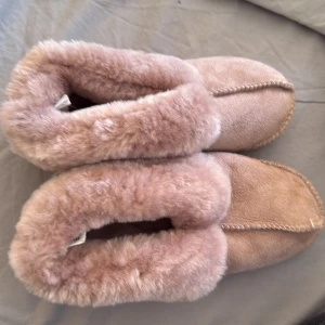 Beiga/rosa fluffiga tofflor - Supermysiga tofflor i beige/rosa med fluffig päls runt öppningen och inuti. Perfekta att glida runt i hemma när det är kallt. Mjukt material och klassisk form med rund tå och platt sula. Endast använda någon enstaka gång.
