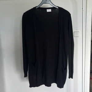 Svart kofta från Vila, lång modell - Svart lång kofta från Vila i storlek XS. Koftan är stickad, har långa ärmar och två fickor framtill. Mjuk och skön känsla med ribbade muddar vid ärmslut och nederkant. Använt flitigt men hängt i garderoben ett tag så den är lite nopprig men det försöker jag ta bort innan jag skickar den💞 PRIS GÅR ATT DISKUTERA!! orginal pris; 350kr