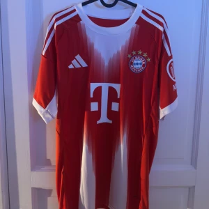Bayern München Olise #17 matchtröja L - Riktigt snygg Bayern München fotbollströja från Adidas i storlek L. Röd med vita detaljer, klubbmärke och sponsortryck på bröstet, samt Olise och nummer 17 på ryggen. Klassiska Adidas-ränder på axlarna och modern design framtill. Slim fit och tillverkad i lätt funktionsmaterial.