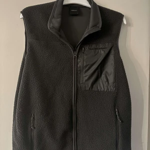 Svart fleeceväst Peak Performance L - Svart fleeceväst från Peak Performance i storlek L. Västen har hög krage, hel dragkedja och tre fickor med dragkedja, varav en bröstficka i blankt material. Perfekt lager-på-lager-plagg med sportig vibe.