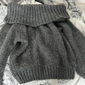 Grå stickad off-shoulder tröja Gina Tricot - Mysig mörkgrå stickad off-shoulder från Gina Tricot i storlek S. Tröjan har en bred, ribbad polokrage och långa ärmar. Perfekt för kyliga dagar och enkel att styla med jeans eller kjol. Har en liten fläck men syns knappt! Så mysig och skön! Älskar färgen❤️