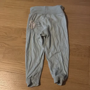 Ljusgrå mjukisbyxor med broderi - Supermjuka ljusgrå mjukisbyxor med bred midja och söt broderad detalj med texten 'Happy little lamb' på ena höften. Perfekta för chill dagar eller som mysplagg hemma.