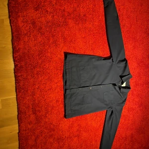 Mörkblå overshirt från Les Deux - Snygg mörkblå overshirt från Les Deux med klassisk krage och tre stora fickor framtill. Jackan har knäppning med knappar och långa ärmar med manschett. Perfekt för lager-på-lager och stilren look.