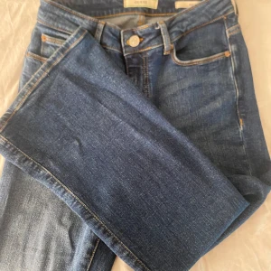 Blå Guess Sexy Flare jeans - Snygga blå jeans från Guess i modellen Sexy Flare. Klassisk femficksdesign, orangea sömmar och ikonisk triangel-logga bak. Jeansen har utsvängda ben och är tillverkade i ett mjukt denimtyg som sitter skönt på kroppen.