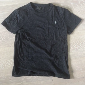 Svart t-shirt från Polo Ralph Lauren - Svart t-shirt från Polo Ralph Lauren med klassisk rund hals och korta ärmar. T-shirten har en broderad vit Polo-logga på bröstet och är gjord i mjuk bomull. Perfekt för en clean och chill stil, enkel att matcha med jeans eller shorts.