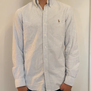 Blårandig skjorta från Polo Ralph Lauren - Snygg blårandig skjorta från Polo Ralph Lauren i slim fit. Klassisk button-down krage, broderad logga på bröstet och vita knappar framtill. Tillverkad i mjuk bomull och har långa ärmar med manschett. Perfekt för en clean och stilren look. Snyggt slitet vid kragen!