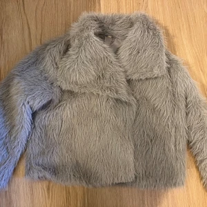 Grå fuskpälsjacka med stor krage - Säljer en fluffig grå pälsjacka med stor krage och långärmade ärmar. Jackan har en oversized look och är tillverkad i mjukt syntetmaterial. Perfekt för dig som vill sticka ut och hålla dig varm under kalla dagar. Den är från shein och tyvärr så är den liten vattenskadad om man säger så.