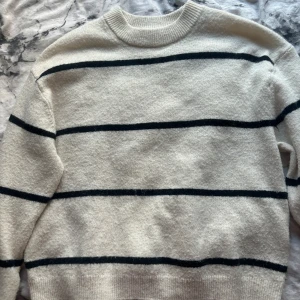 Randig stickad tröja från H&M XS - Krämvit stickad tröja från H&M i storlek XS med svarta horisontella ränder. Tröjan har rund halsringning, ribbade muddar och lång ärm. Perfekt för dig som gillar en enkel men snygg stil med lite retrovibbar.