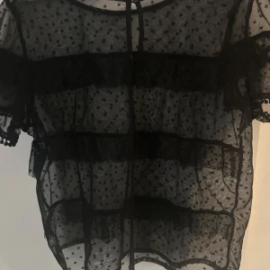Svart transparent prickig blus - Säljer en svart transparent blus med korta ärmar och prickigt mönster. Blusen har volangdetaljer och passar perfekt för finare tillfällen💕. Vet itne vart den kommer ifrån men skulle gissa Zara och den är i storlek XS🥰