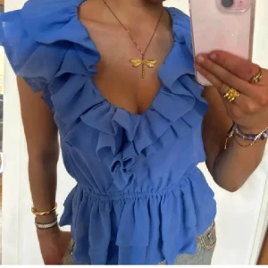 Supertrendig volangblus från H&M i blått  - Supersöt och eftertraktad blus från H&M med volanger längs ringningen och axlarna. Blusen är ärmlös, har markerad midja och flera lager volanger nertill. Perfekt för dig som gillar romantisk och trendig stil. Storlek 40 men passar mer som en 36/38. Har även en exakt likadan i samma storlek! Skriv vid frågor 💞