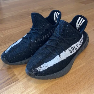 Adidas Yeezy Boost 350 V2 svart/vit - Säljer ett par Adidas Yeezy Boost 350 V2 i svart med vit stripe och SPLY-350 text på sidan. Skorna är använda men fortfarande i bra skick säljer dom för dom inte passar länge. Äkta med kvitto ingen har boxen också nånstans 