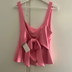 Rosa topp med rosett från Zara - Supersöt rosa topp från Zara som jag själv aldrig använt för att storleken inte passade mig, därav sitter prislappen kvar. Toppen har breda axelband och stor rosett baktill. Toppen har en lätt utsvängd form vid midjan och dragkedja i sidan för enkel påklädning. 