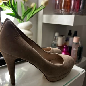 Beige mockapumps från Bronx - Snygga pumps i beige mocka från Bronx med rund tå och hög klack. Skorna har en klassisk och stilren design med plattform framtill för extra komfort. Perfekta för dig som vill ha en elegant look med en neutral färg som passar till det mesta.