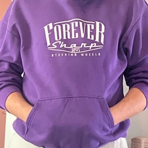 Lila hoodie Forever Sharp storlek L - Säljer en lila hoodie från Forever Sharp med stor vit text och coolt tryck på ryggen med en skeletfigur som surfar bland hajar. Hoodien har huva, magficka och ribbade muddar. Perfekt för dig som vill sticka ut med en färgstark och unik stil.