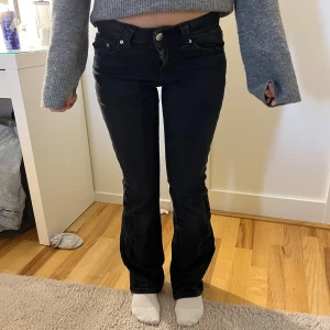 Svarta bootcut jeans - Säljer ett par svarta jeans från Gina Tricot med bootcut-modell och snygga fickor med lock och knappar bak. Jeansen har låg midja.