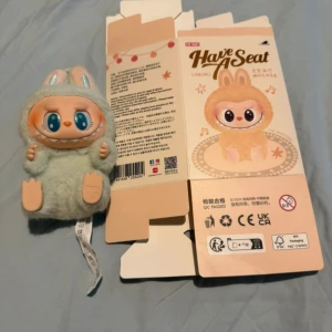 Have A Seat Labubu - Upptäck den söta och fluffiga figuren Labubu från 'Have A Seat'! Perfekt för dig som gillar gulliga samlarobjekt och vill ha något unikt på hyllan. Med stora blå ögon och mjuk päls är den ett måste för alla som älskar kawaii och roliga figurer. Authentic Have a Seat Labubu. Ququ from Paris Popmart with scannable QR code.  #popmart #keychain #pendant #labubu #blindbox   labubu keychain, collectible plush, Paris popmart, adorable pendant, cutesy charm, scannable QR code, limited edition, character