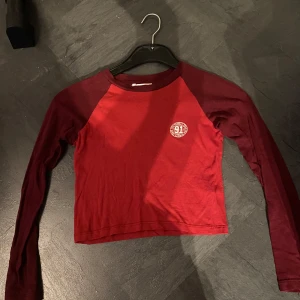 Långärmad croppad tröja - Säljer en röd långärmad croppad tröja från Varsity Team. Tröjan har en rund halsringning och är gjord i mjuk bomull, har en lite sportig look.